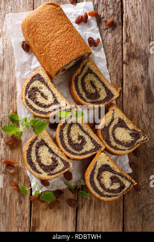 De délicieuses pâtisseries poppy rouleau avec raisins secs, noix décorées à la menthe close-up sur une table en bois. Haut Vertical Vue de dessus Banque D'Images