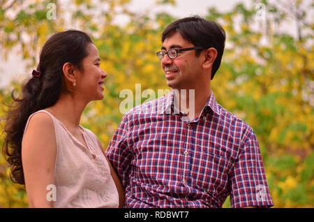 Un jeune couple indien souriant se tenant contre les feuilles jaunes d'amaltas pendant l'été, en automne à New Delhi, en Inde Banque D'Images