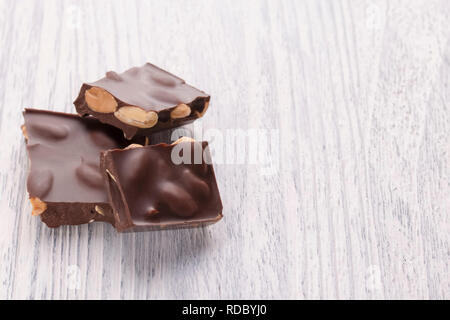 Tranches de chocolat noir délicieux avec des noix sur une table en bois blanc. Les cadres macro Banque D'Images