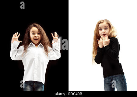 Le portrait de deux heureux surpris filles sur un fond studio blanc et noir. Les émotions humaines concept. La comparaison. L'enfance, sourire, bonheur, joie, kid, l'amitié concept Banque D'Images