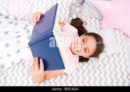 Lit enfant fille lay read book vue d'en haut. Encourager les habitudes utiles.Kid se préparer à aller au lit. Temps agréable dans une chambre confortable. Kid fille cheveux longs pyjamas mignons vous détendre et lire livre. Satisfait de professionnels. Banque D'Images