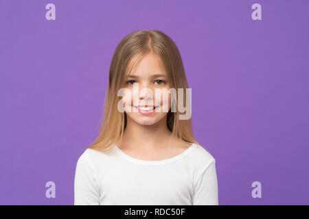 Fille avec beau sourire isolé sur fond violet. Avec l'enfant mignon visage studio portrait. Modèle avec cheveux blonds brillant et les yeux verts. Kid en cavalier blanc s'amusant, enfance heureuse concept. Banque D'Images