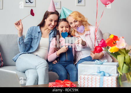 Grand-mère, mère et fille à la célébration festive de caps hugging prendre des photos avec des coeurs papier selfies Banque D'Images