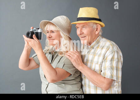 Touristes en chapeaux de plage studio isolés sur gray man hugging woman taking photos avec l'appareil photo Banque D'Images