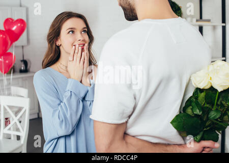 Portrait of a young man holding bouquet de roses derrière back while smiling girlfriend en attente de surprise Banque D'Images