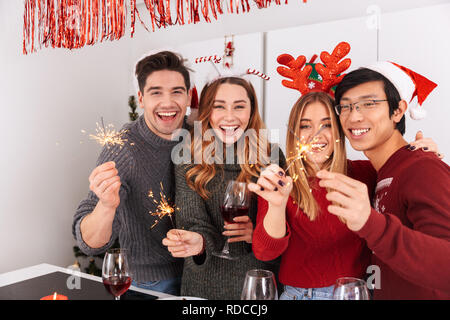 Groupe de gens tenant multiethnique de fête avec vin et verres étincelants, tout en célébrant la nouvelle année en télévision Banque D'Images