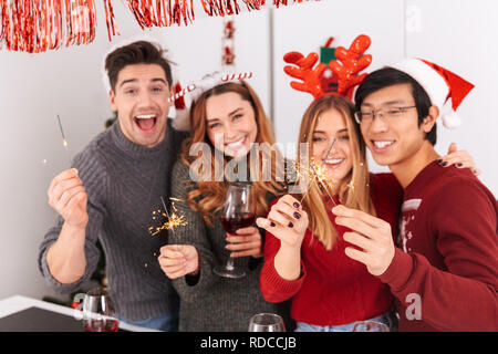 Groupe de personnes multiethnique heureux holding glasses avec vin et cierges tout en célébrant la nouvelle année en télévision Banque D'Images