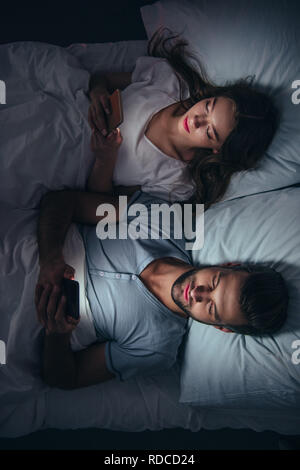 Young couple Lying in Bed and using smartphones la nuit Banque D'Images