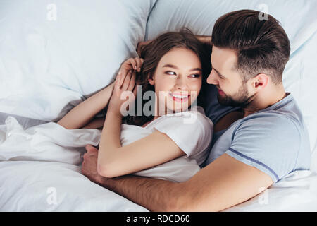 Jeune couple aimant hugging doux au lit et à la recherche dans les yeux Banque D'Images