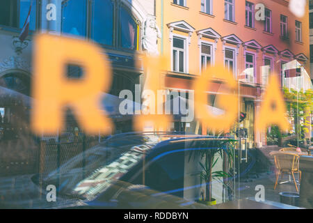 L'inscription Riga sur la fenêtre avec un reflet de la vie dans les rues de la vieille ville un jour d'été Banque D'Images