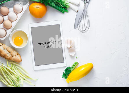 Digital touch screen tablet avec des légumes frais et des ustensiles de cuisine sur l'arrière-plan, Vue de dessus Banque D'Images
