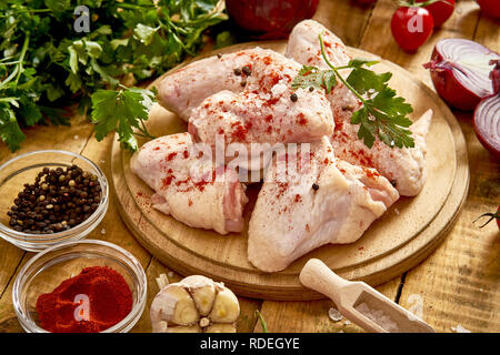 Ailes de poulet frais biologique sur une planche avec des épices et des légumes sur la vieille table en bois. Banque D'Images