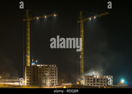 Grues à tour et à plusieurs étages inachevé de hauts bâtiments en construction au chantier éclairé la nuit sur Banque D'Images