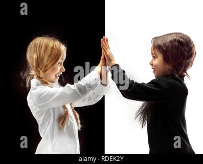 Agiter la main et cinq de haut. Le portrait de deux professionnels se tenant la main les filles sur un fond studio blanc et noir. Les émotions humaines concept. La comparaison. L'enfance, sourire, bonheur, joie, kid, l'amitié concept Banque D'Images