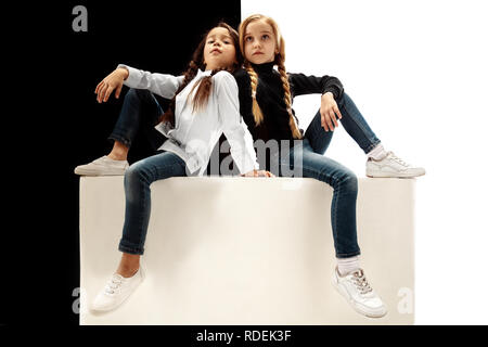 Le portrait de deux seriouus triste filles sur un fond studio blanc et noir. Les émotions humaines concept. La comparaison. L'enfance, sourire, bonheur, joie, kid, l'amitié concept Banque D'Images