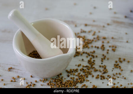 Les graines de coriandre dans un mortier en porcelaine sur la table en bois blanc, Banque D'Images