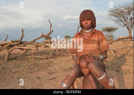 Jeune femme Hamar avec coiffure traditionnelle en argile rouge dans ses cheveux et avec son enfant, la vallée de la rivière Omo, dans le sud de l'Éthiopie Banque D'Images