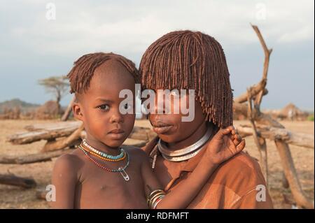 Jeune femme Hamar avec coiffure traditionnelle en argile rouge dans ses cheveux et son enfant, la vallée de la rivière Omo, dans le sud de l'Éthiopie Banque D'Images