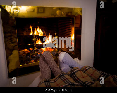 Close up image de couple sous la couverture par cheminée réchauffe pieds en bas de laine se détendre avec une tasse de boisson chaude à la maison dans le froid wi Banque D'Images