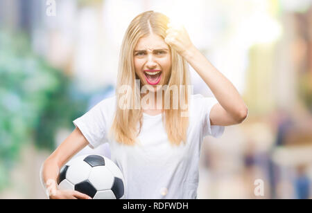 Belle jeune femme blonde holding soccer ball sur fond isolé contrarié et frustré de crier avec colère, fou et hurler avec ha Banque D'Images