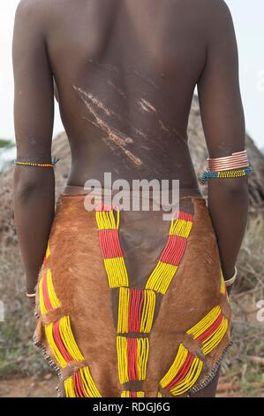 Jeune femme Hamar avec coiffure traditionnelle et d'argile rouge avec des cicatrices et les marques d'être fouetté sur le dos Banque D'Images