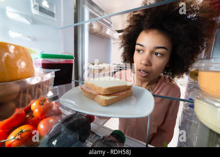 Close-up d'une jeune femme africaine à la recherche de nourriture dans un réfrigérateur Banque D'Images