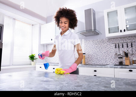 Happy African Young Woman Cleaning Spray Cuisine sale compteur avec un détergent et de serviette jaune Banque D'Images