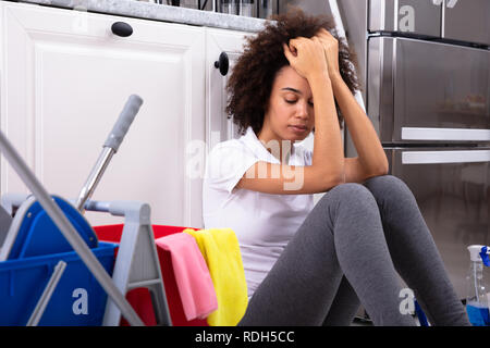 Épuisé African Young Woman Sitting on Floor dans la cuisine Banque D'Images