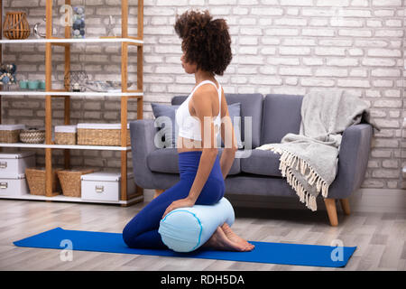 Jeune femme assise sur le tapis d'exercice en équilibre sur le coussin Dans Le Salon Banque D'Images