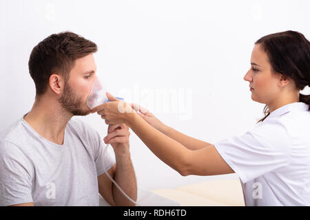 Side View of young female Doctor Holding masque à oxygène sur la bouche du patient de sexe masculin Banque D'Images