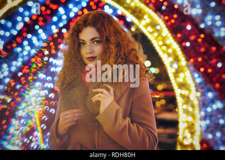 Belle jeune fille aux cheveux roux. Portrait sur la nuit rue de la ville. Bokeh de lumières de fête. Banque D'Images