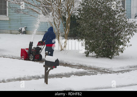 Mâle adulte à l'aide de la souffleuse à neige rouge on sidewalk Banque D'Images