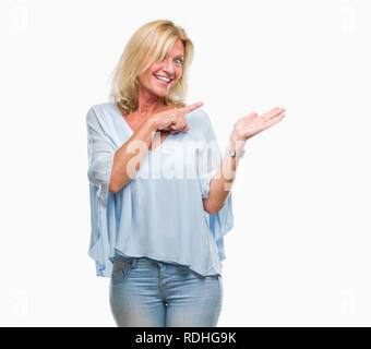 L'âge moyen d'affaires blonde femme de plus fond isolé surpris et souriant à la caméra tout en présentant avec la main et en pointant avec le doigt. Banque D'Images