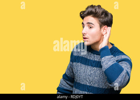 Jeune homme séduisant sur fond isolé smiling with hand sur l'écoute d'une oreille pour entendre des rumeurs ou ragots. Concept de la surdité. Banque D'Images