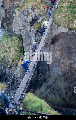 Le comté d'Antrim / Irlande du Nord - 28 déc 2016 : Groupe de touristes traversant le célèbre pont de corde sur la côte nord de l'Irlande du Nord, Royaume-Uni Banque D'Images
