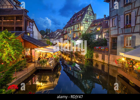 Colmar, France. Maisons à pans de bois et vérandas de restaurants se reflétant dans l'eau au crépuscule dans la Petite Venise salon Banque D'Images