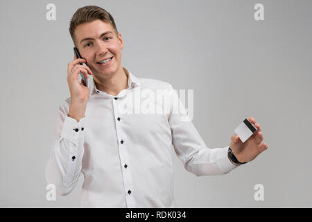 Portrait of young man talking on mobile phone avec carte de crédit en main isolé sur fond blanc Banque D'Images