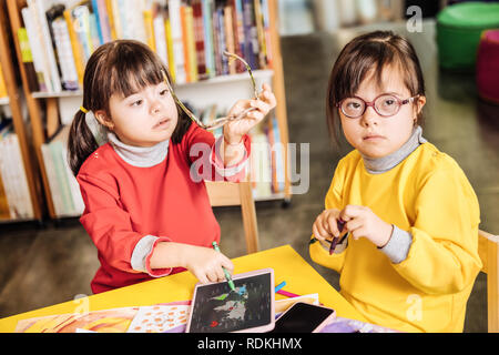 Fille avec le syndrome de assis près de sa sœur en tenant lunettes Banque D'Images