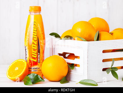 Londres, Royaume-Uni - 15 janvier 2019 : Bouteille en plastique de soda orange Lucozade soft drink avec des matières d'oranges dans boîte en bois. Banque D'Images