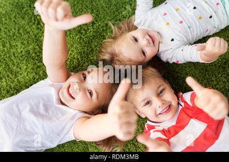 Happy kids lying on floor et showing Thumbs up Banque D'Images