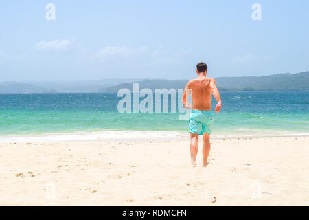 Homme qui courait pieds nus sur la plage dans l'océan turquoise sur une île, la mer des Caraïbes Banque D'Images