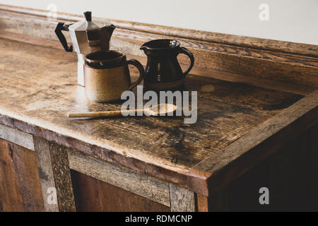 High angle close up de la machine à expresso, tasse de faïence et cruche et cuillère en bois sur bois vintage armoire de cuisine. Banque D'Images