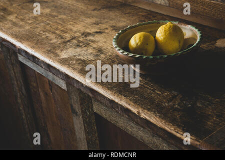 High angle portrait de deux citrons dans un bol de faïence sur armoire de cuisine en bois vintage. Banque D'Images