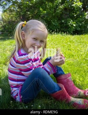 Fille blonde avec petit canard assis sur l'herbe en plein air Banque D'Images