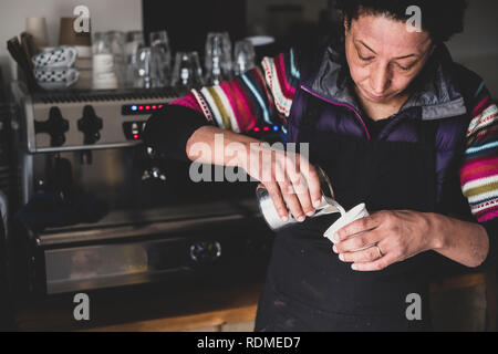 Femme derrière machine à expresso verser du lait chaud en papier. Banque D'Images