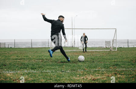 footballeur frappant un tir de pénalité. Joueur de football donnant un coup de pied dans le ballon vers le poteau de but avec le gardien de but en position. Banque D'Images