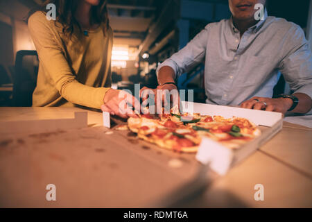 collègues d'affaires partageant une pizza tard dans la nuit au bureau. Plan recadré d'un couple mangeant de la pizza assis ensemble. Banque D'Images