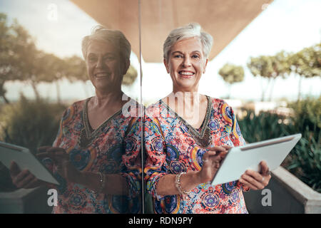 Portrait d'une belle d'âge moyen aux cheveux gris smiling woman working with tablet à la recherche dans l'appareil photo Banque D'Images