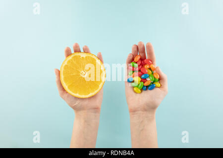 Comprimés de vitamines et de jus d'orange dans les mains, vue d'en haut. Les mains tenant des fruits dans une main et bouquet de bonbons dans l'autre en arrière-plan simple Banque D'Images