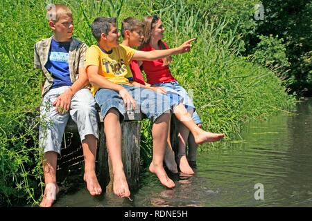 Des enfants assis sur un quai dans un ruisseau et qui traînent leurs jambes dans l'eau, Bad Bodenteich, Basse-Saxe Banque D'Images